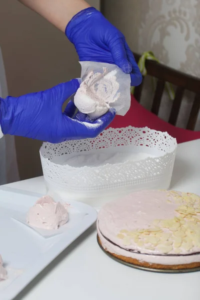 A woman prepares a marshmallow cake. Makes roses from marshmallows for decoration and places on the cake. Works with a mask and gloves.