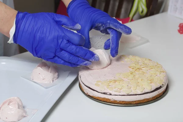 A woman prepares a marshmallow cake. Makes roses from marshmallows for decoration and places on the cake. Works with a mask and gloves.