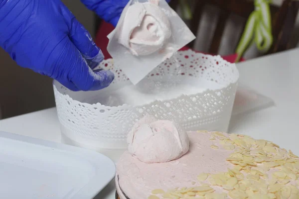 A woman prepares a marshmallow cake. Makes roses from marshmallows for decoration and places on the cake. Works with a mask and gloves.