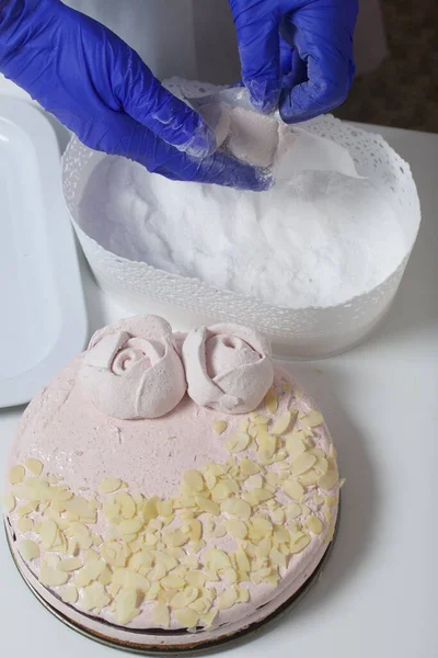 A woman prepares a marshmallow cake. Makes roses from marshmallows for decoration and places on the cake. Works with a mask and gloves.