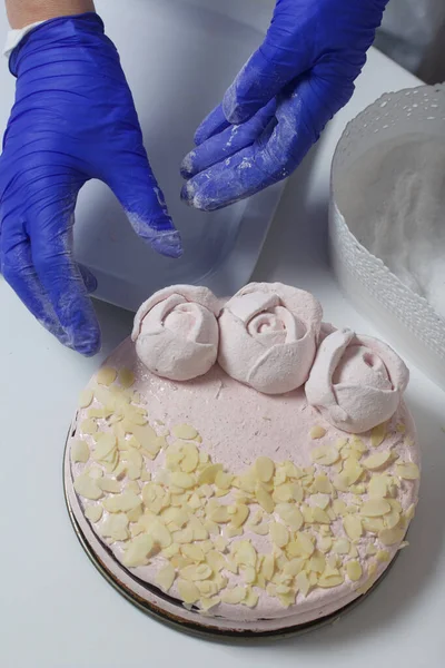 A woman prepares a marshmallow cake. Makes roses from marshmallows for decoration and places on the cake. Works with a mask and gloves.