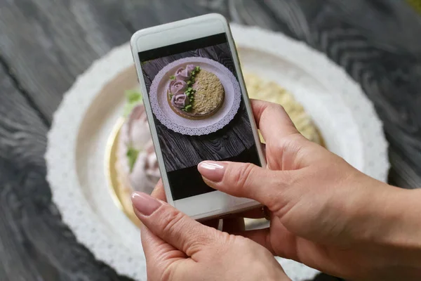 A woman photographs a marshmallow cake. The cake is decorated with marshmallow roses and almond petals.