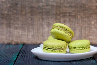Açık yeşil badem kurabiyeleri bir çay tabağının üzerinde. Çam ağacından kalasların üzerinde gevrek ahşap bir dokuyla.