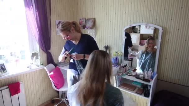 Penata rambut memotong rambut wanita di rumah. Seorang wanita duduk di kursi di depan cermin. Pembuat videonya tercermin di cermin. Penata rambut adalah seorang pengusaha individual — Stok Video