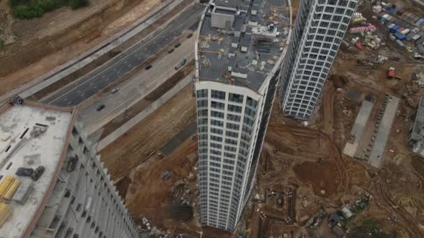 Moderne stedelijke ontwikkeling. Bouwplaats met meerdere verdiepingen in aanbouw. De bouw is aan de gang. De toppen van de gebouwen zijn zichtbaar. Aan de horizon is een woonwijk — Stockvideo