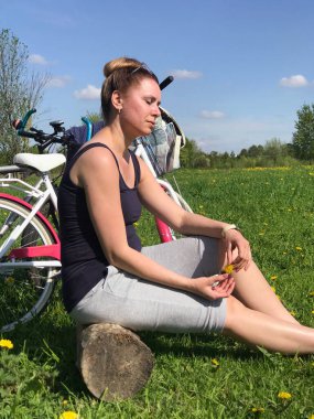 Kadın ahşap bir kütüğün üzerinde oturuyor. Bahar çayırında. Yakınlarda bisikletler var. Kendini izole ederken dinlen..