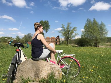 Kadın büyük bir taşın üzerinde oturuyor. Bahar çayırında. Yakınlarda bisikletler var. Kendini izole ederken dinlen..