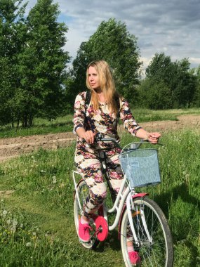 Bisiklet üzerinde poz veren eşofmanlı bir kız. Parktaki çimenlikte.