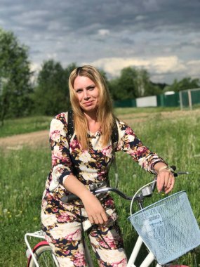 Bisiklet üzerinde poz veren eşofmanlı bir kız. Parktaki çimenlikte.