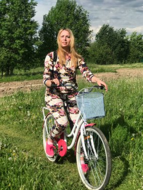 Bisiklet üzerinde poz veren eşofmanlı bir kız. Parktaki çimenlikte.