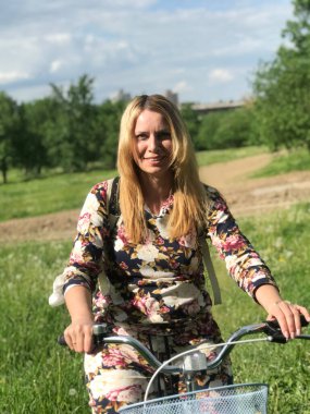 Bisiklet üzerinde poz veren eşofmanlı bir kız. Parktaki çimenlikte.