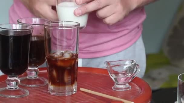 Faire un latte glacé bleu. Un homme ajoute de la crème à un verre de boisson. Il y a d'autres ingrédients sur le comptoir à côté. Gros plan. — Video