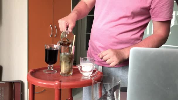 Faire un latte glacé bleu. Des ingrédients masculins dans un verre. A proximité se trouve un ordinateur portable sur lequel il regarde une recette. — Video