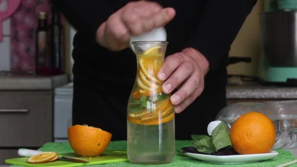Εμφιαλωμένο νερό εμποτισμένο με πορτοκάλι και βασιλικό. Ο άνθρωπος βάζει ένα σωλήνα σε αυτό. Συνταγές νερού αποτοξίνωσης. — Αρχείο Βίντεο