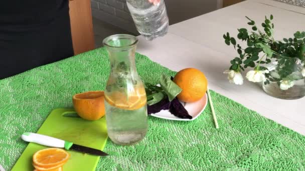 Ένας άντρας κόβει ένα πορτοκάλι και το βάζει σε ένα μπουκάλι νερό. Νερό εμποτισμένο με πορτοκάλι και βασιλικό. Συνταγές αποτοξίνωσης νερού. Πυροβολήθηκε από το πλάι.. — Αρχείο Βίντεο