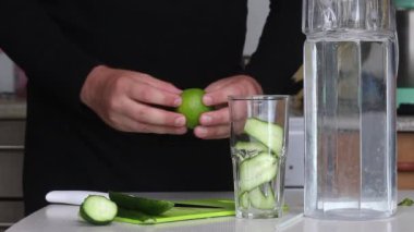 Bir adam limon kesiyor. Yakınlarda bir sürahide su var. Limon ve salatalık ile karıştırılmış pişirme suyu. Detoks su tarifi. Yakın çekim..