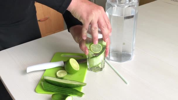 Mannen lägger halmen i ett glas med skivad lime och gurka. Matlagningsvatten genomsyras av lime och gurka. Detox vatten recept. — Stockvideo