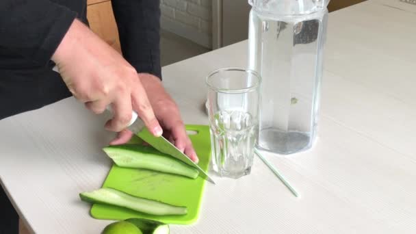 En man skär en gurka. Närliggande kalk och vatten i en karaff. Matlagningsvatten genomsyras av lime och gurka. Detox vatten recept — Stockvideo