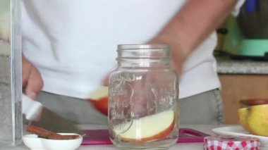 Adam elmaları parçalara ayırıp kavanoza atıyor. Detoks suyu hazırlanıyor. Elma, tarçın ve anason. Elma ve baharatla karıştırılmış pişirme suyu. Yakın çekim..