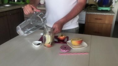 Bir adam dilimlenmiş elma ve baharatlara su döker. Detoks suyu hazırlanıyor. Elma, tarçın ve anason. Elma ve baharatla doldurulmuş yemek suyu..