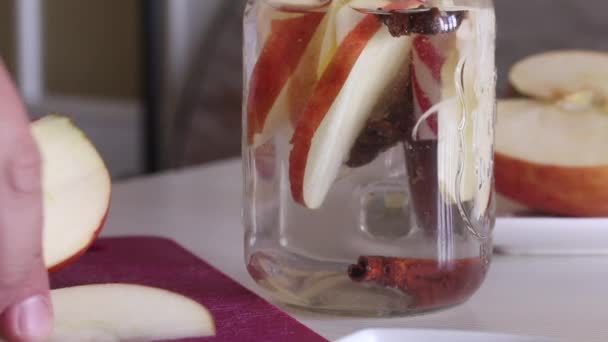 Un hombre arroja manzanas y especias en rodajas en un frasco de agua. Preparando agua de desintoxicación. De manzanas, canela y anís. Agua de cocción infundida con manzanas y especias. Primer plano de disparo. — Vídeo de stock