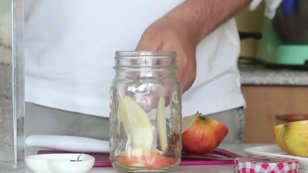 Un homme verse de l'eau dans des pommes et des épices tranchées. Préparation de l'eau de désintoxication. De pommes, cannelle et anis. Eau de cuisson infusée de pommes et d'épices. Gros plan. — Video