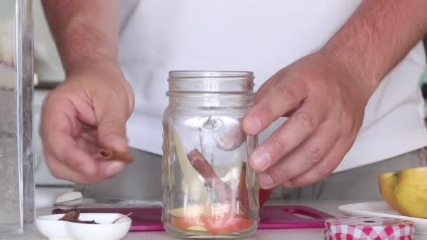 Un hombre añade especias a un frasco de manzanas en rodajas. Preparando agua de desintoxicación. De manzanas, canela y anís. Agua de cocción infundida con manzanas y especias. Primer plano de disparo. — Vídeo de stock