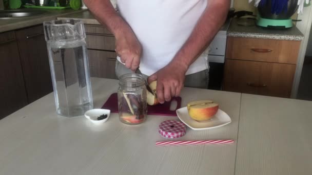 Ο άνθρωπος κόβει τα μήλα και τα προσθέτει στο βάζο μπαχαρικών. Ετοιμάζω νερό αποτοξίνωσης. Από μήλα, κανέλα και γλυκάνισο. Μαγειρικό νερό εμποτισμένο με μήλα και μπαχαρικά. — Αρχείο Βίντεο