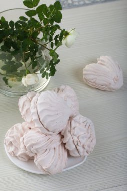 Tabakta ev yapımı marşmelov. Farklı şekillerde şekerlemeler, klasik ve kalp şeklinde. Yakınlarda bir buket gül var..