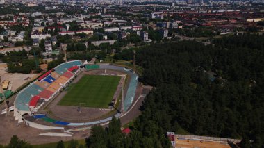 Şehir parkındaki futbol stadyumu. Yakınlarda yeni bir arena inşa ediliyor. Yeşil bir alan ve stantlar görülebilir, farklı renklerde boyanmış. Hava fotoğrafçılığı.