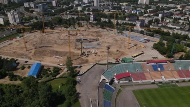 Voetbalstadion in het stadspark. In de buurt wordt een nieuwe arena gebouwd. Een groen veld en standaards zijn zichtbaar, geschilderd in verschillende kleuren. Zijwaarts vliegen. Luchtfotografie. — Stockvideo
