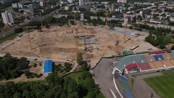 Football stadium in the city park. A new arena is being built nearby. A green field and stands are visible, painted in different colors. Flying sideways. Aerial photography — Vídeo de Stock