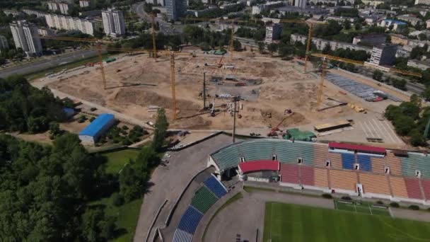 Football stadium in the city park. A new arena is being built nearby. A green field and stands are visible, painted in different colors. Aerial photography — Video