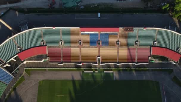 Stade de football dans le parc de la ville. Un champ vert et des stands sont visibles, peints en différentes couleurs. Survolez les gradins. Photographie aérienne — Video
