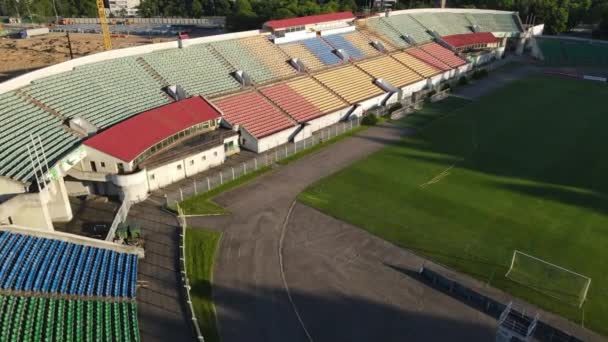 市内公園内のサッカースタジアム。緑のフィールドとスタンドが表示され、異なる色で塗装されます。スタンドの上を飛行。空中写真. — ストック動画