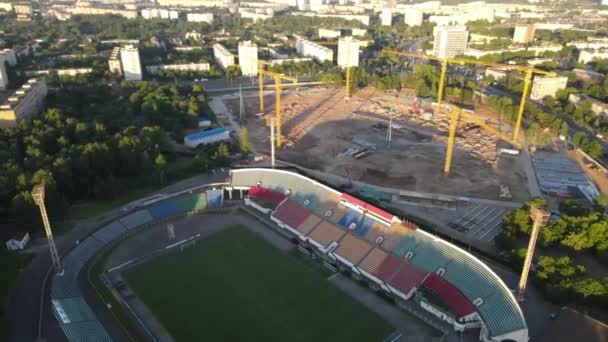 市内公園内のサッカースタジアム。緑のフィールドとスタンドが表示され、異なる色で塗装されます。上昇する太陽の光の中で弧を描いて飛んでいます。空中写真 — ストック動画