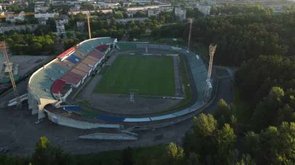 Stade de football dans le parc de la ville. Un champ vert et des stands sont visibles, peints en différentes couleurs. Aux rayons du soleil levant. Photographie aérienne. — Video