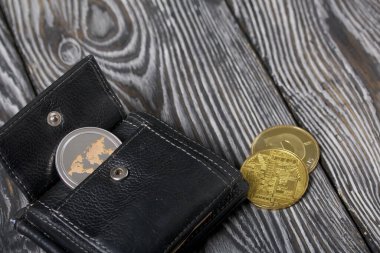 Açık bir cüzdanda kripto para. Yakınlarda diğer kripto para birimlerinin paraları var. Çam ağacından yapılmış tahtalarda.