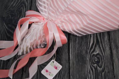 Buket folyo ve el işi kağıdına sarılı. Kurdeleler ve etiketler görünür. Sevdiklerine bir hediye..