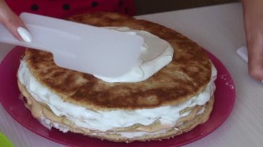 Bir kadın pasta katmanlarının üstüne krema sürüyor, üst üste istifliyor. Pasta yapmak için gerekli malzemeler..