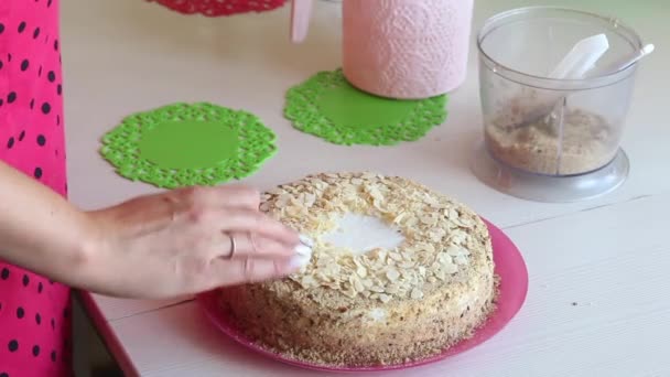 Egy nő mandulaszirmokkal díszíti a tortát. A torta rétegeit krém borítja. Közelkép. — Stock videók