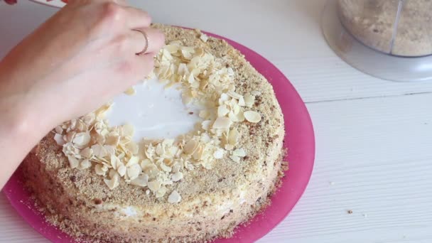 Egy nő mandulaszirmokkal díszíti a tortát. A torta rétegeit krém borítja. Közelkép.. — Stock videók