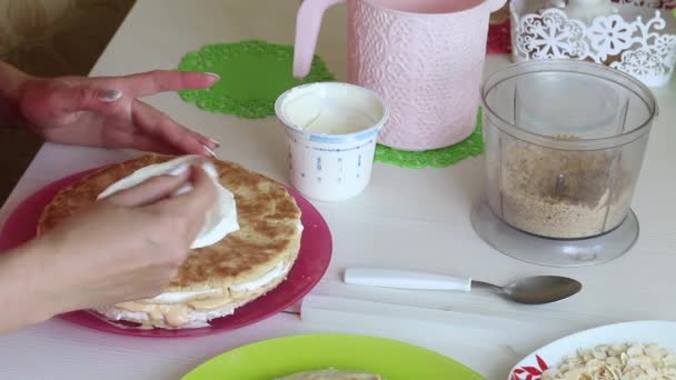De vrouw stapelt de taartlagen op elkaar. Smeer ze met room. In de buurt ingrediënten voor het maken van de taart. van bovenaf gefilmd.. — Stockvideo
