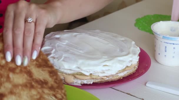 La mujer está apilando las capas de pastel una encima de la otra. Grasa el pastel con crema. Ingredientes cercanos para hacer el pastel. — Vídeo de stock