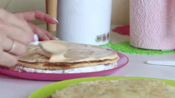 La mujer está apilando las capas de pastel una encima de la otra. Los lubrica con crema. Ingredientes cercanos para hacer el pastel. — Vídeo de stock