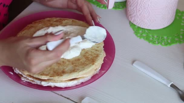 La mujer está apilando las capas de pastel una encima de la otra. Los lubrica con crema. Ingredientes cercanos para hacer el pastel. Filmado desde arriba. — Vídeos de Stock