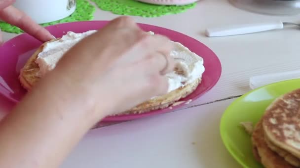 Egy nő krémet keneget a tortarétegekre. Közelkép a kezéről és a tortáról. Hátulról filmezve. — Stock videók