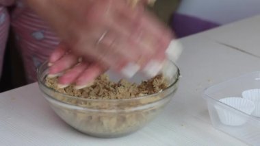 Bir kadın fıstık ezmesi, çikolata ve hindistan cevizi unundan toplar yapar. Sağlıklı tatlılar hazırlar. Masanın yanında kâğıt şekerli tartlar var. Yakın çekim.