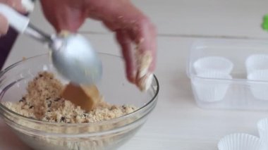 Bir kadın şeker yapmak için fıstık ezmesi, çikolata ve hindistan cevizi unu karıştırıyor. Masanın yanında kâğıt şekerli tartlar var. Yakın çekim...