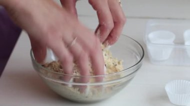 Bir kadın şeker yapmak için fıstık ezmesi, çikolata ve hindistan cevizi unu karıştırıyor. Masanın yanında kâğıt şekerli tartlar var. Yakın çekim.